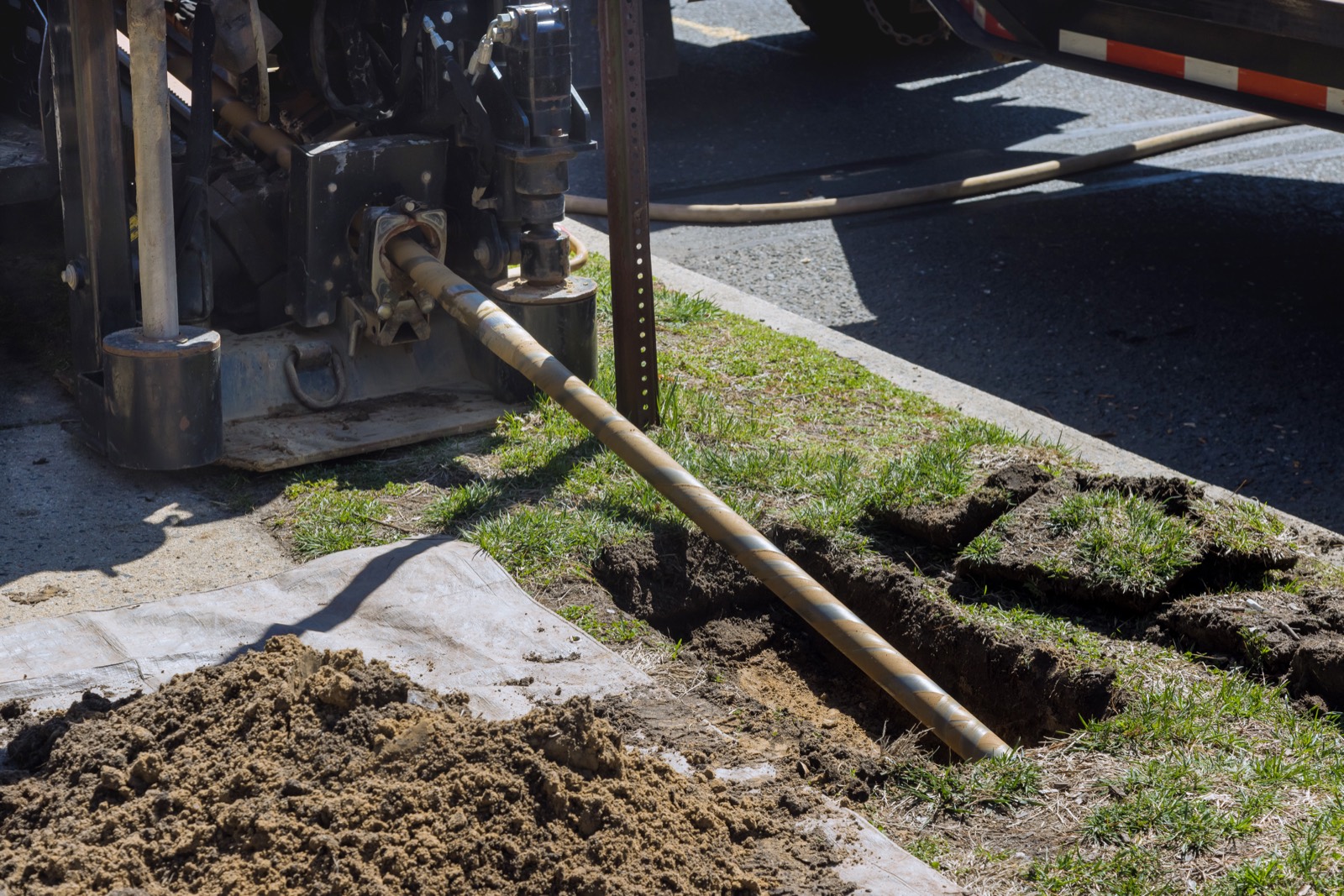 Trenchless directional drilling rod entering the ground beside a roadway